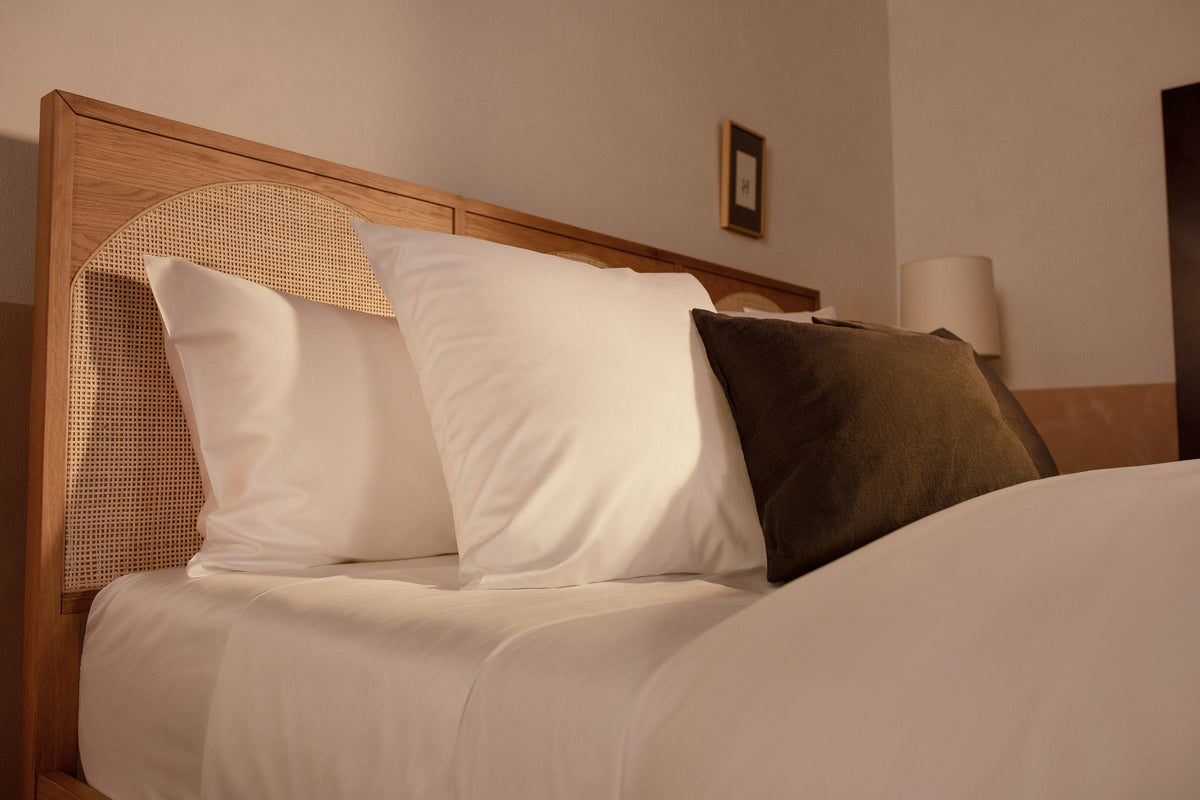 An close up image of Americano Cotton Sateen pillows in white on a bed with a charcoal velvet throw pillow. data-image-id=