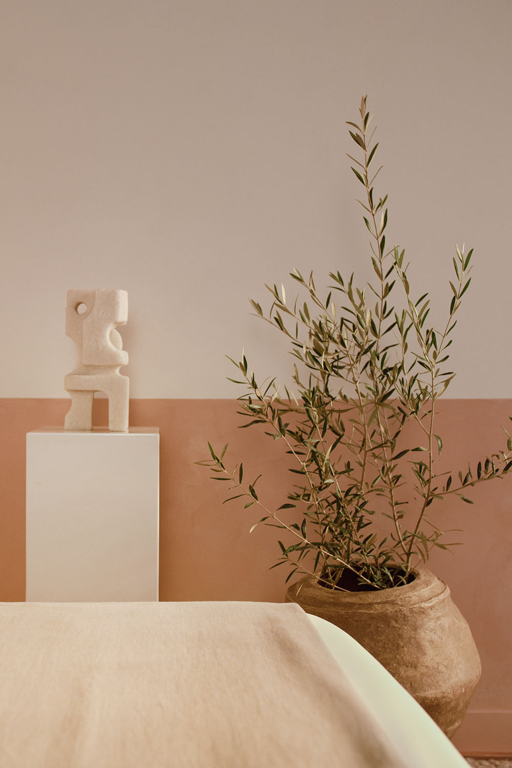 Image of foot of bed with small decorative statue and olive tree in pot against wall.