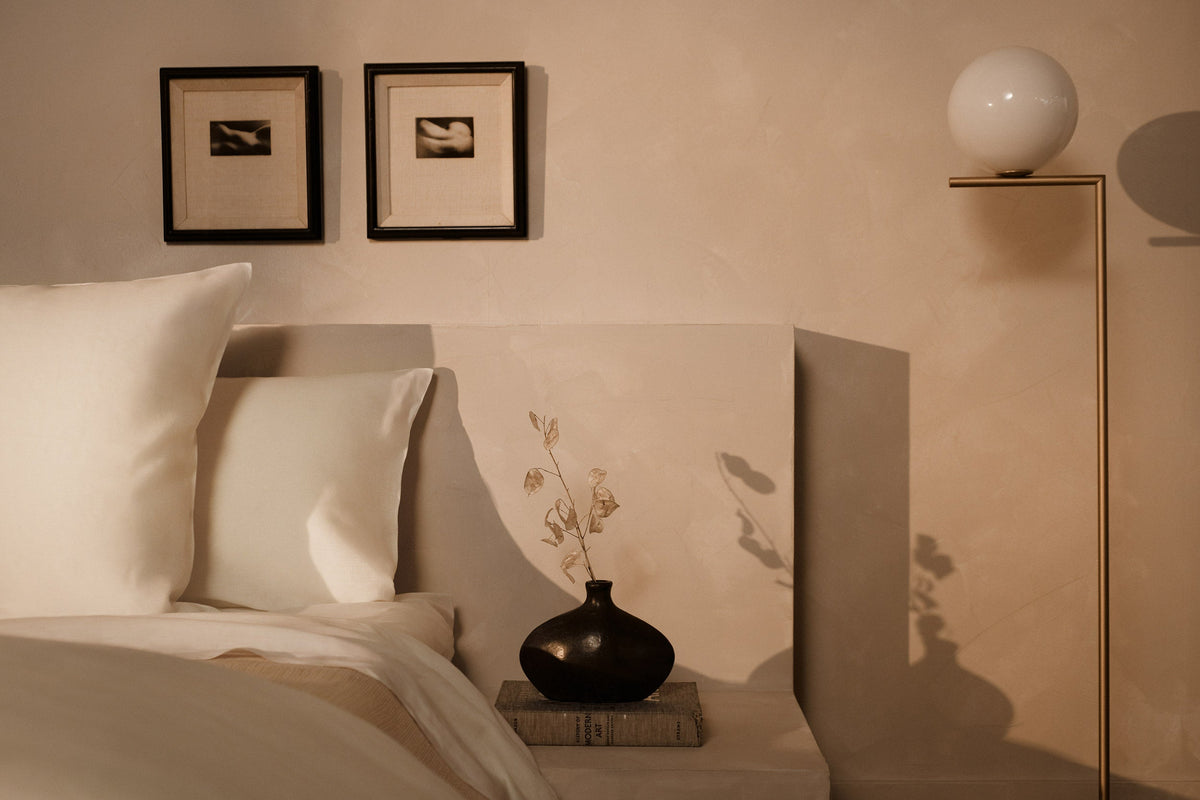 An image of LETTO Lino Primo 100% linen pillows next to a nightstand with a black vase and flowers. data-image-id=