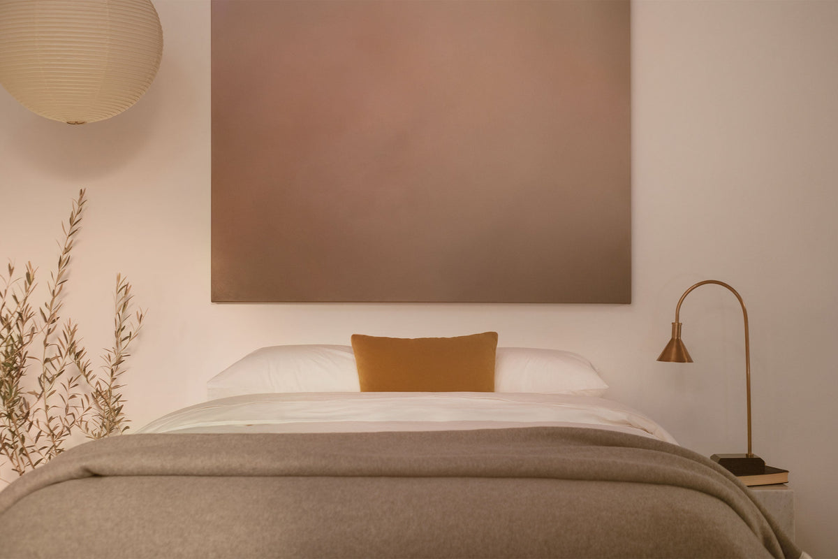 A bedroom with contemporary art and a platform bed made in LETTO 100% Organic Cotton Percale sheets, a gray Monte Bianco cashmere blanket, and orange velvet throw pillow. data-image-id=