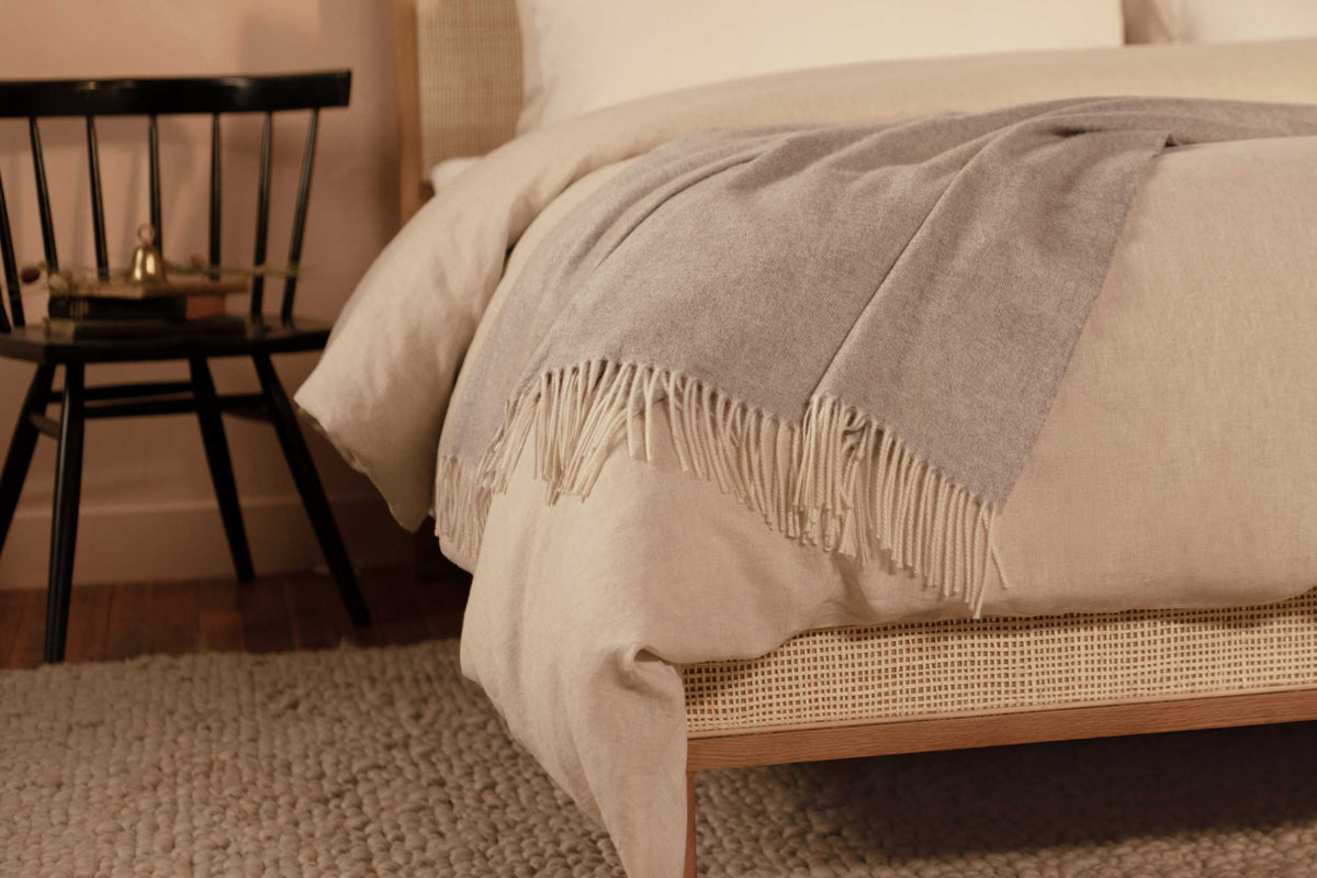 Close up image of the LETTO Coccola 100% cashmere woven throw blanket in light gray draped at the foot of a bed. data-image-id=