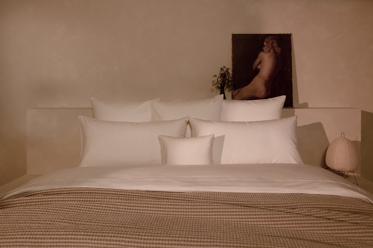 A bedroom with a luxuriously made bed in LETTO Sea Island Cotton Percale sheets and duvet cover in color white, with a Nido cotton waffleweave blanket in gray. data-image-id=