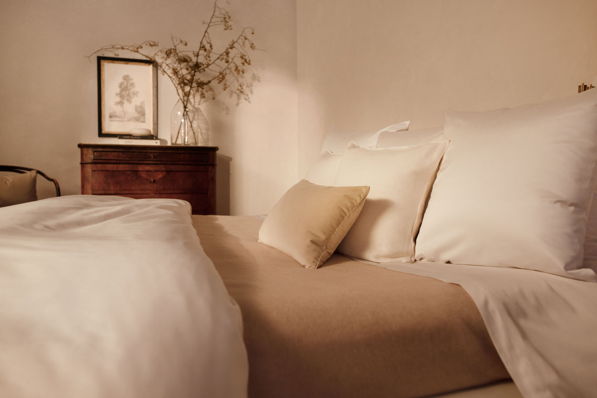 A close up image of LETTO Sea Island Cotton Sateen pillows in white on a bed with a cream colored Monte Bianco cashmere blanket. data-image-id=