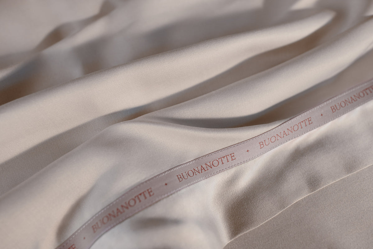 A close up image of the Buonanotte ribbon on the bottom edge of smooth and silky LETTO Woodland Silk beechwood modal flat sheet in color white. data-image-id=
