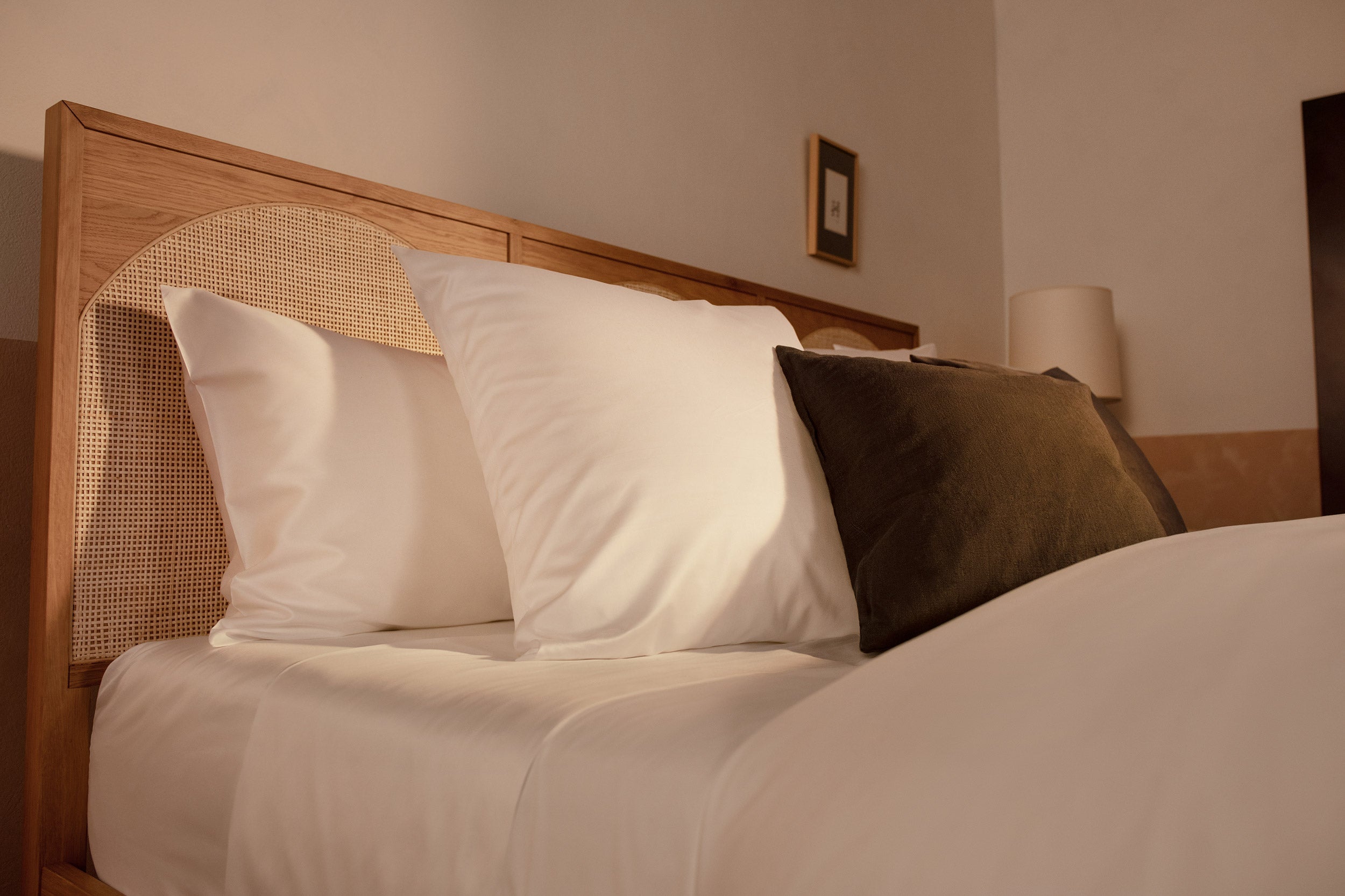 An close up image of Americano Cotton Sateen pillows in white on a bed with a charcoal velvet throw pillow.