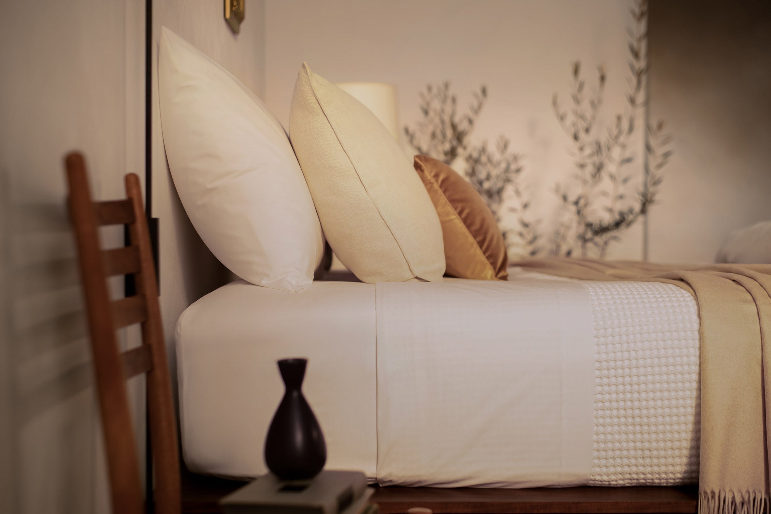 A close up picture of a bed made with LETTO White Classic Cotton Percale sheets and duvet cover, with a Nido waffleweave blanket in white and a tan velvet throw pillow. 