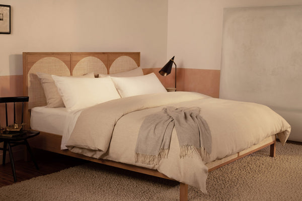 A contemporary bed made with white Classic Linen sheets and a Classic Linen duvet cover in color Natural. The sheets are made of Belgian linen and woven in Italy. The bed has a light gray Coccola cashmere throw blanket draped at the foot of the bed.