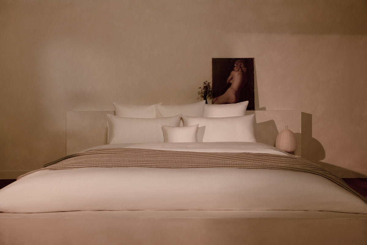 A bedroom with a luxuriously made bed in LETTO Sea Island Cotton Percale sheets and duvet cover in color white, with a Nido cotton waffleweave blanket in gray. data-image-id=