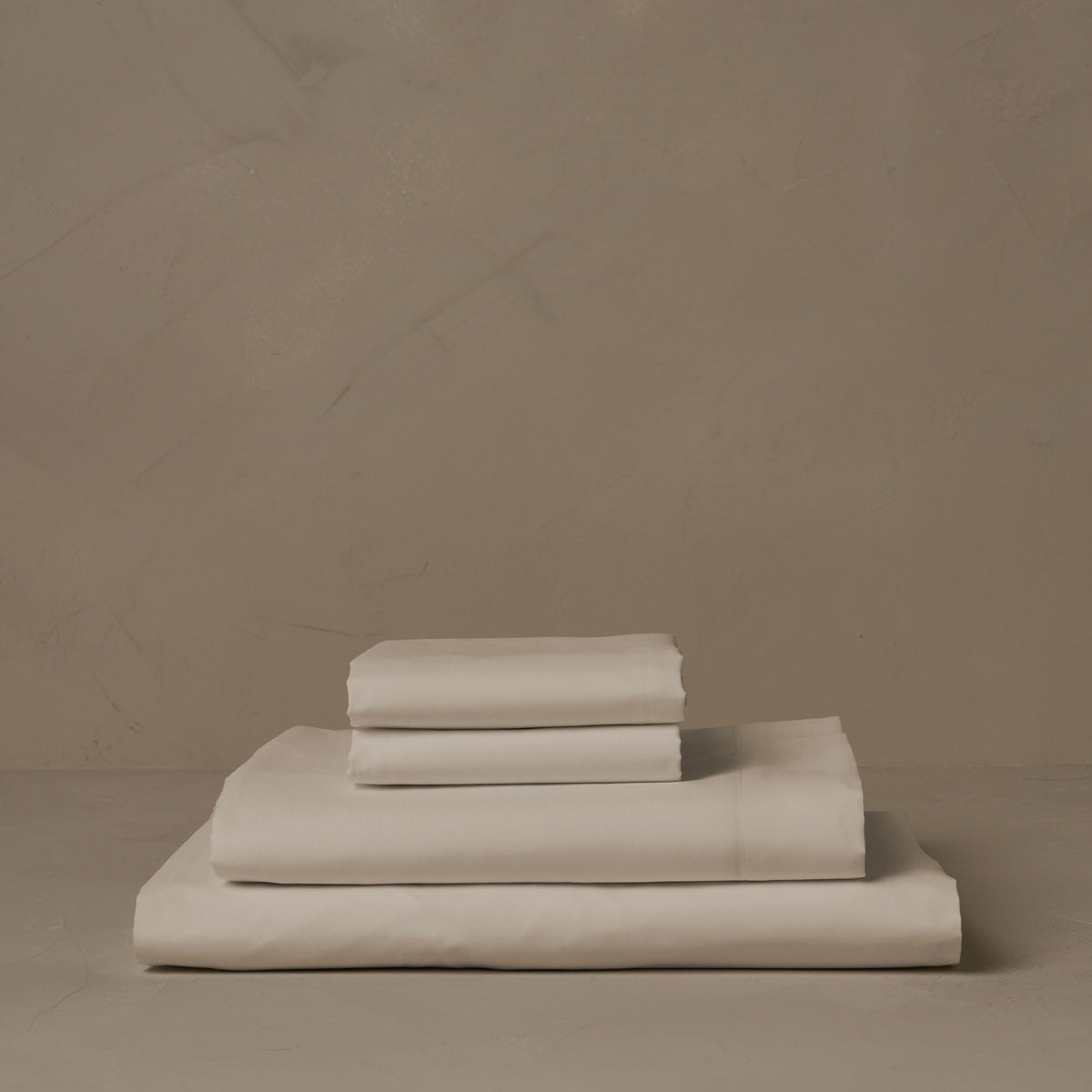 A stack of crisp and cool ivory Americano Cotton Percale sheets.  The sheets are made in Italy of American cotton. The set includes a fitted sheet, a flat sheet, and a pair of pillowcases. data-image-id=