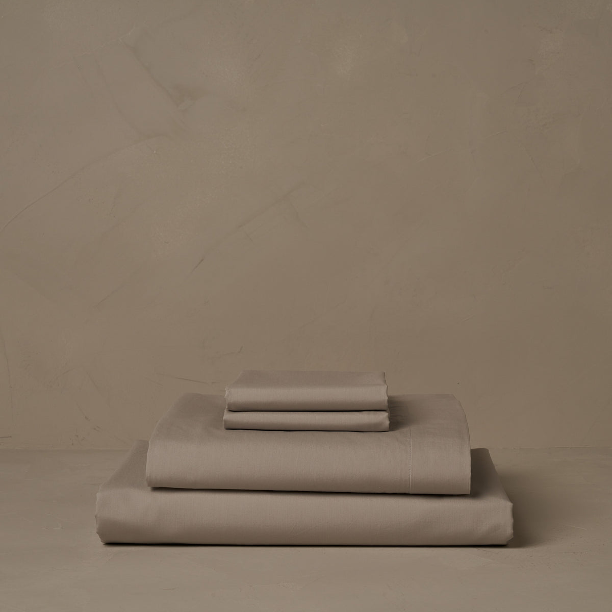 A stack of crisp and cool LETTO Classic Cotton Percale sheets in color gray, made in Italy. The sheet set includes a fitted sheet, a flat sheet, and a pair of pillowcases. data-image-id=