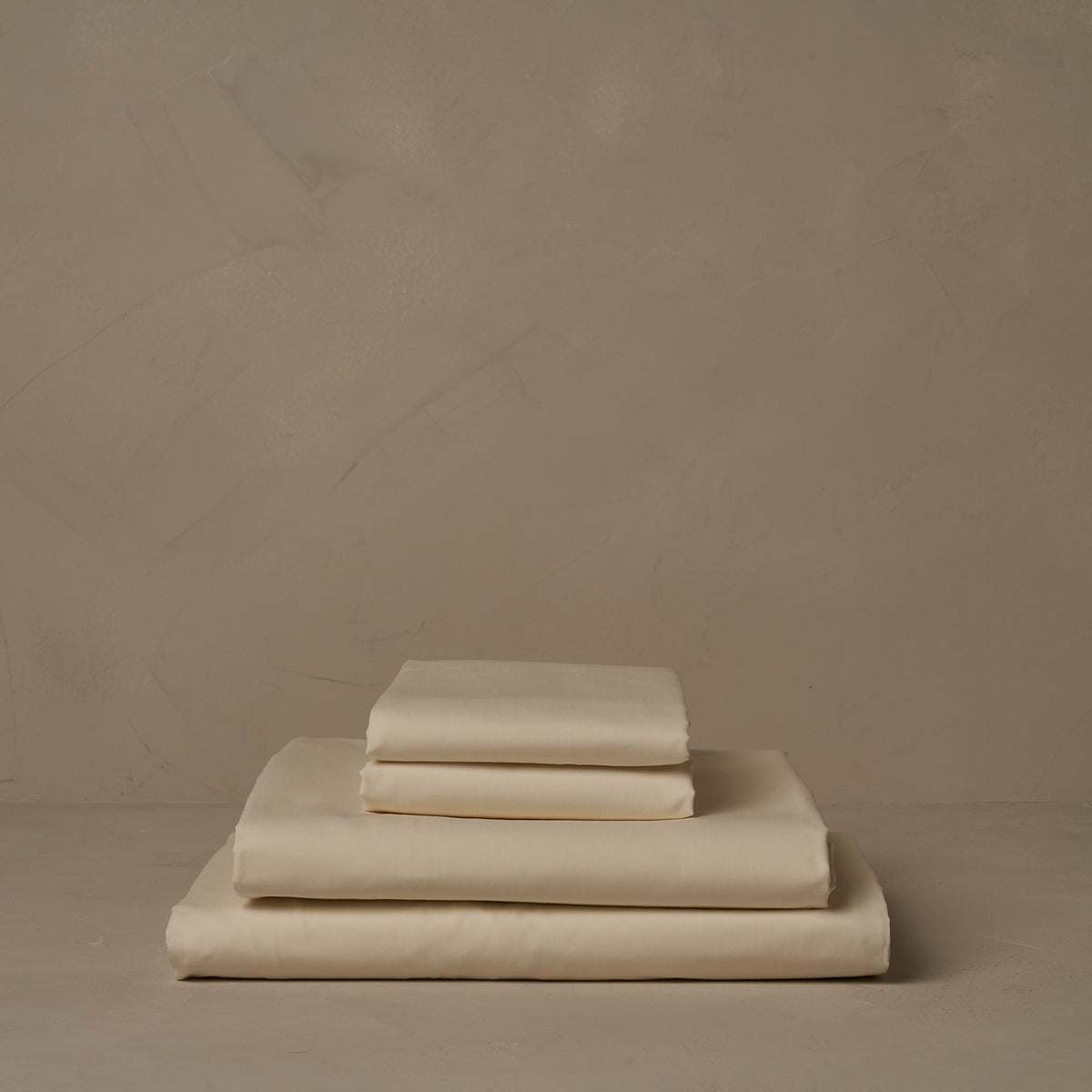 A stack of crisp and cool LETTO Classic Cotton Percale sheets in color ivory, made in Italy. The sheet set includes a fitted sheet, a flat sheet, and a pair of pillowcases. data-image-id=
