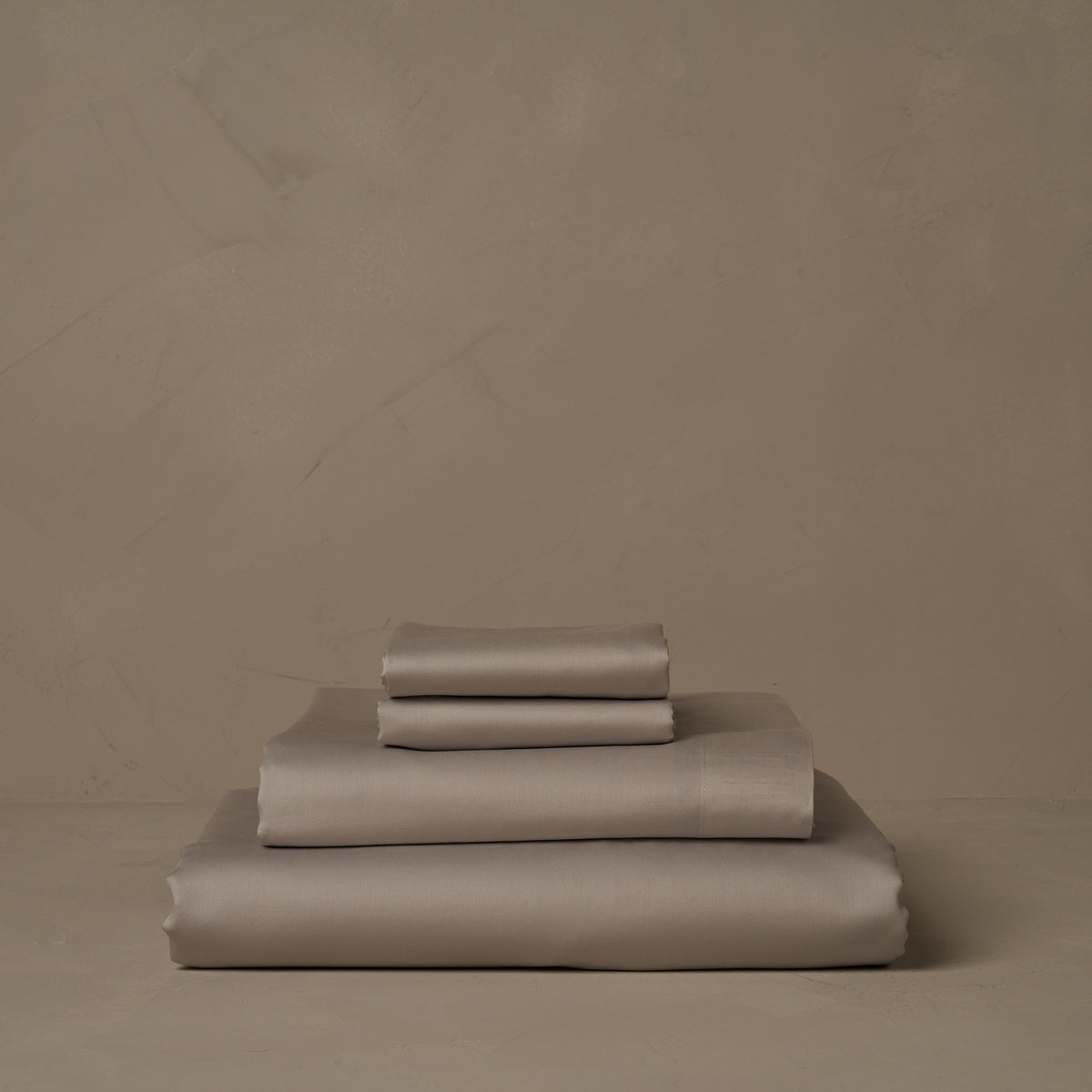 A stack of warm and buttery Classic Cotton Sateen sheet sets in gray, made in Italy. The sheet set includes a fitted sheet, a flat sheet, and a pair of pillowcases. data-image-id=
