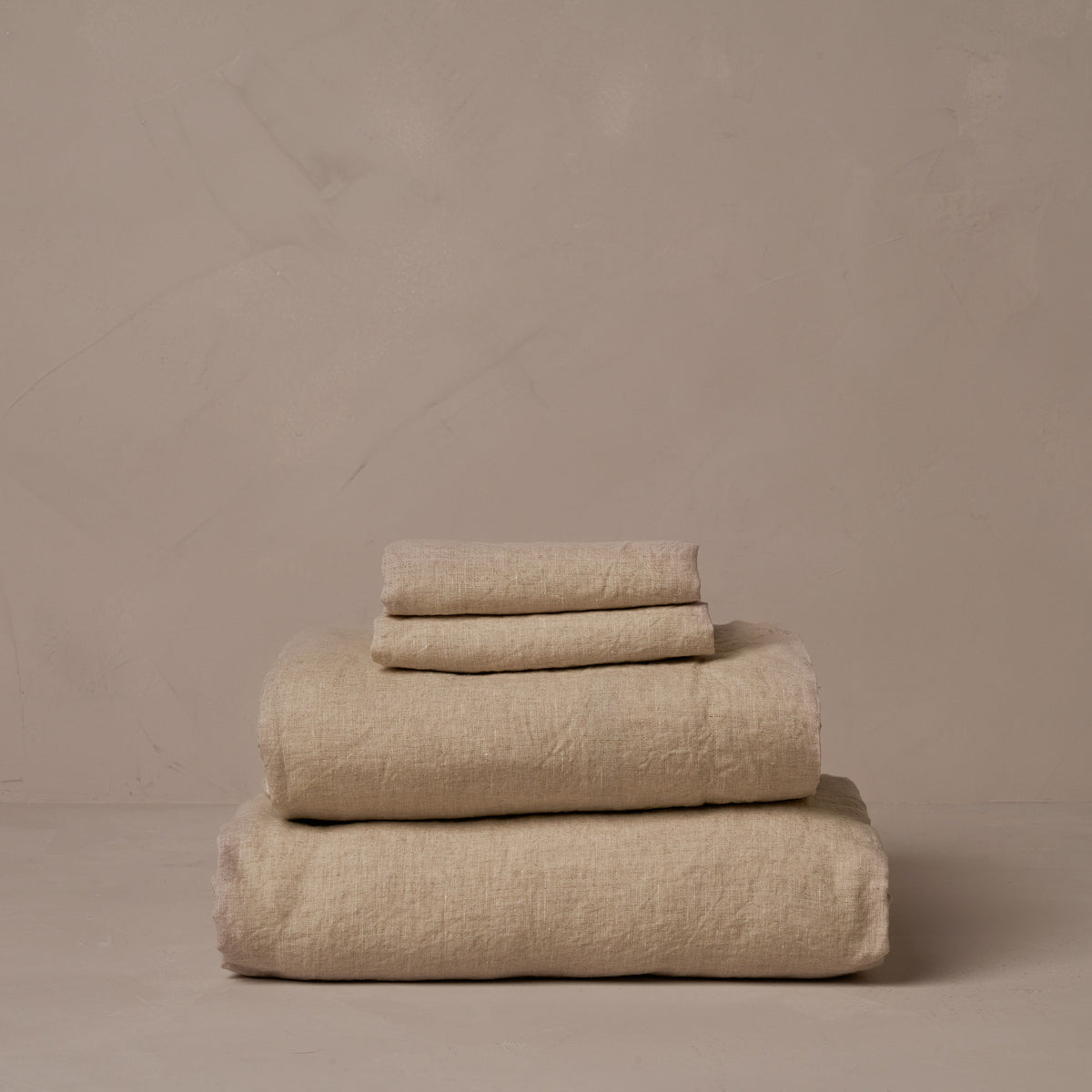 A stack of relaxed and breathable natural colored Classic Linen sheets. Belgian flax, made in Italy. The set includes a fitted sheet, a flat sheet, and a pair of pillowcases. data-image-id=