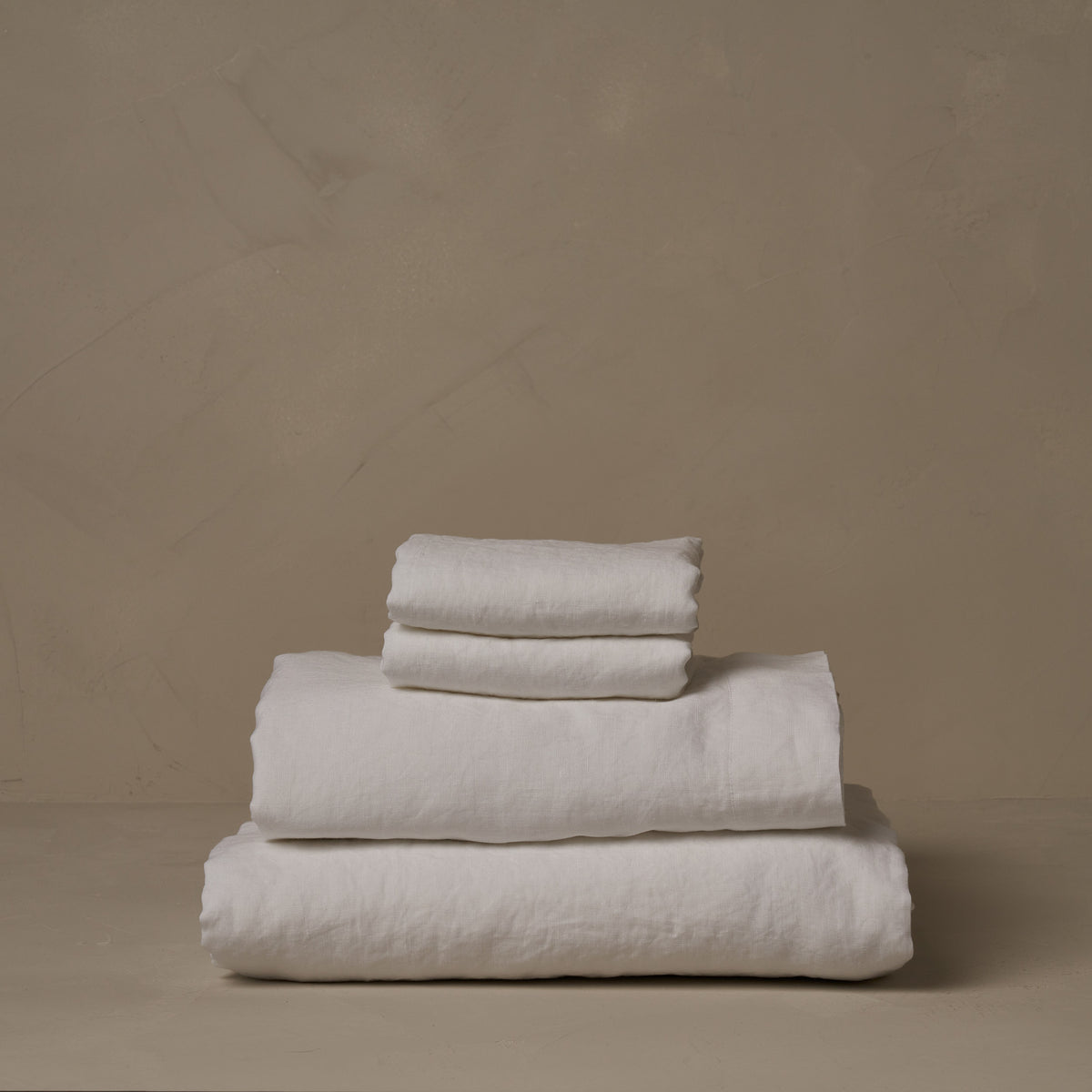 A stack of relaxed and breathable white Classic Linen sheets. Belgian flax, made in Italy. The set includes a fitted sheet, a flat sheet, and a pair of pillowcases. data-image-id=