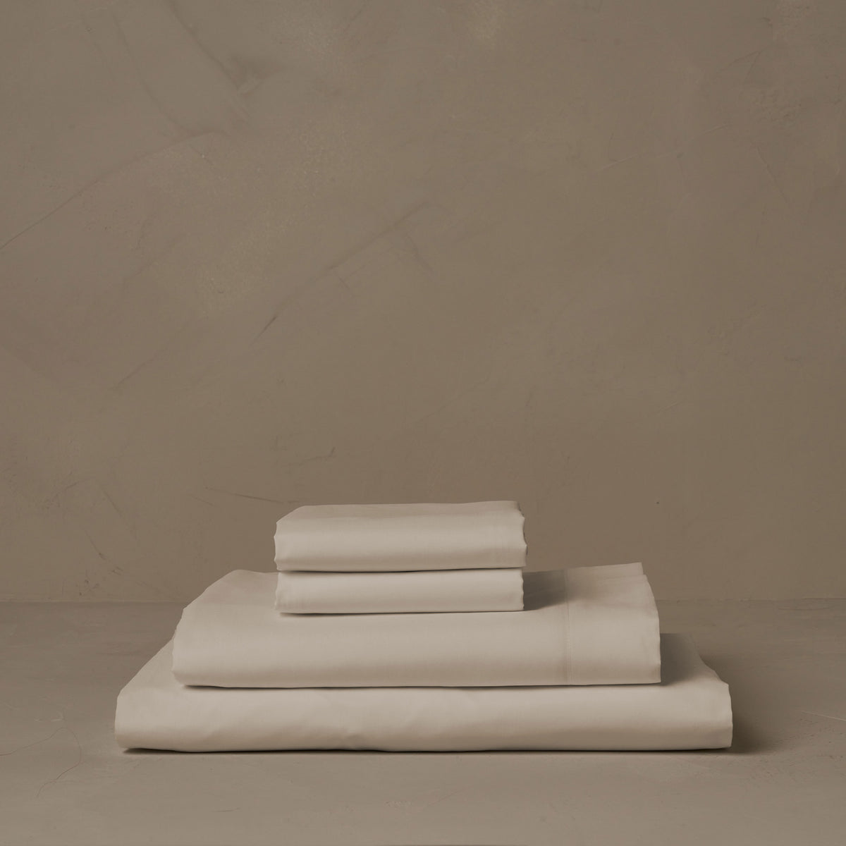 A stack of cool and crisp LETTO Giza Reserve Cotton Percale sheets in ivory, made in Italy. The sheet set includes a fitted sheet, a flat sheet, and a pair of pillowcases. data-image-id=