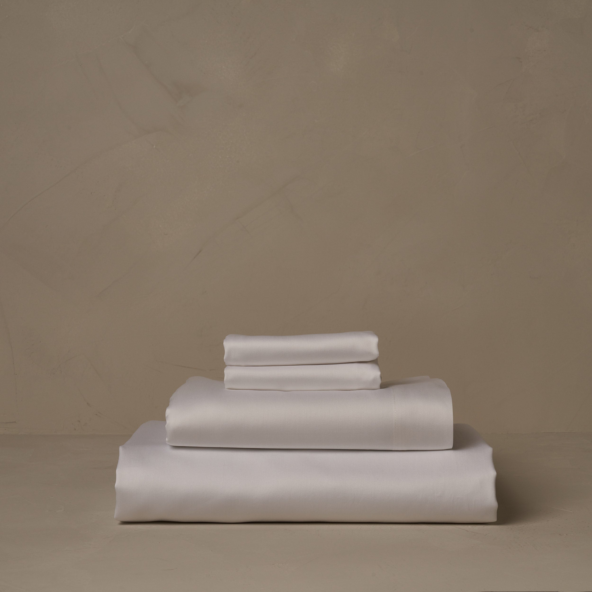 A stack of warm and buttery LETTO Giza Reserve Cotton Sateen sheets in white, made in Italy. The sheet set includes a fitted sheet, a flat sheet, and a pair of pillowcases.