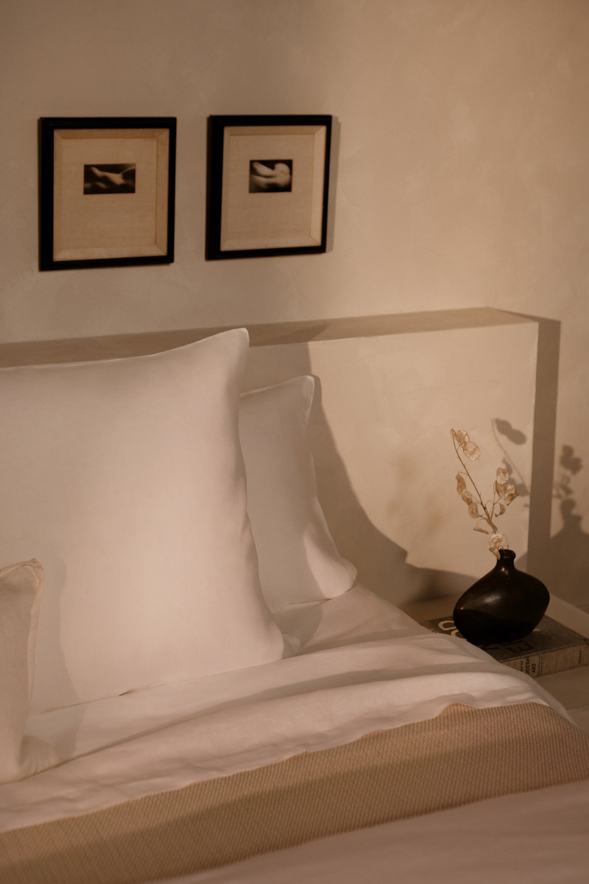 An image of LETTO Lino Primo 100% linen pillows next to a nightstand with a black vase and flowers. data-image-id=