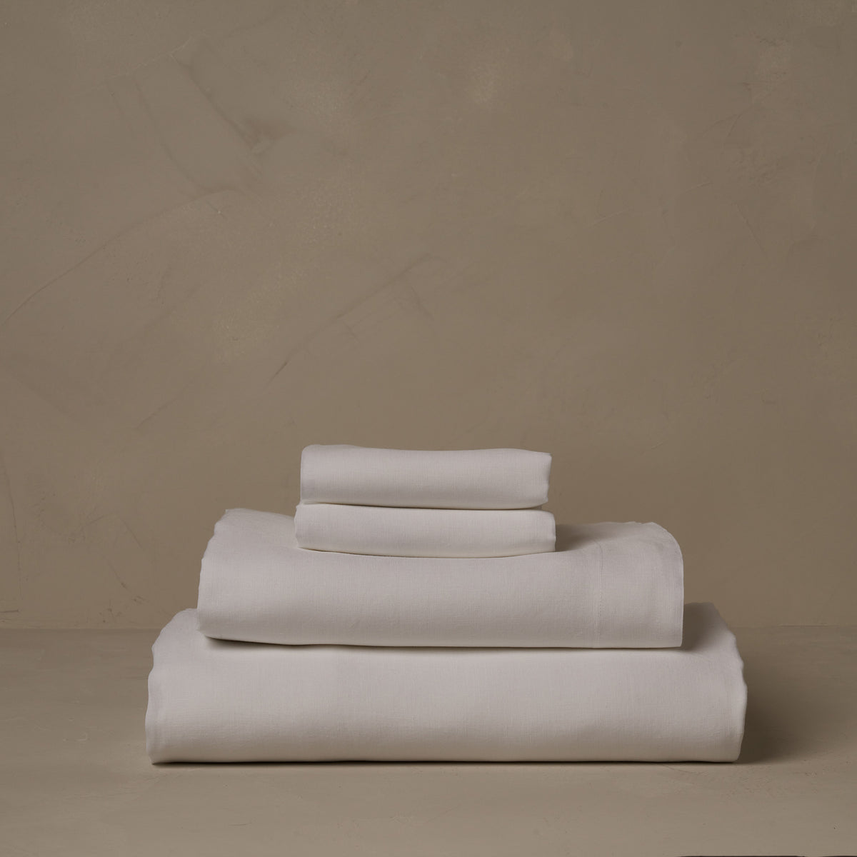 A stack of breathable and relaxed 100% linen LETTO Lino Primo sheets in white, made in Italy. The sheet set includes a fitted sheet, a flat sheet, and a pair of pillowcases. data-image-id=