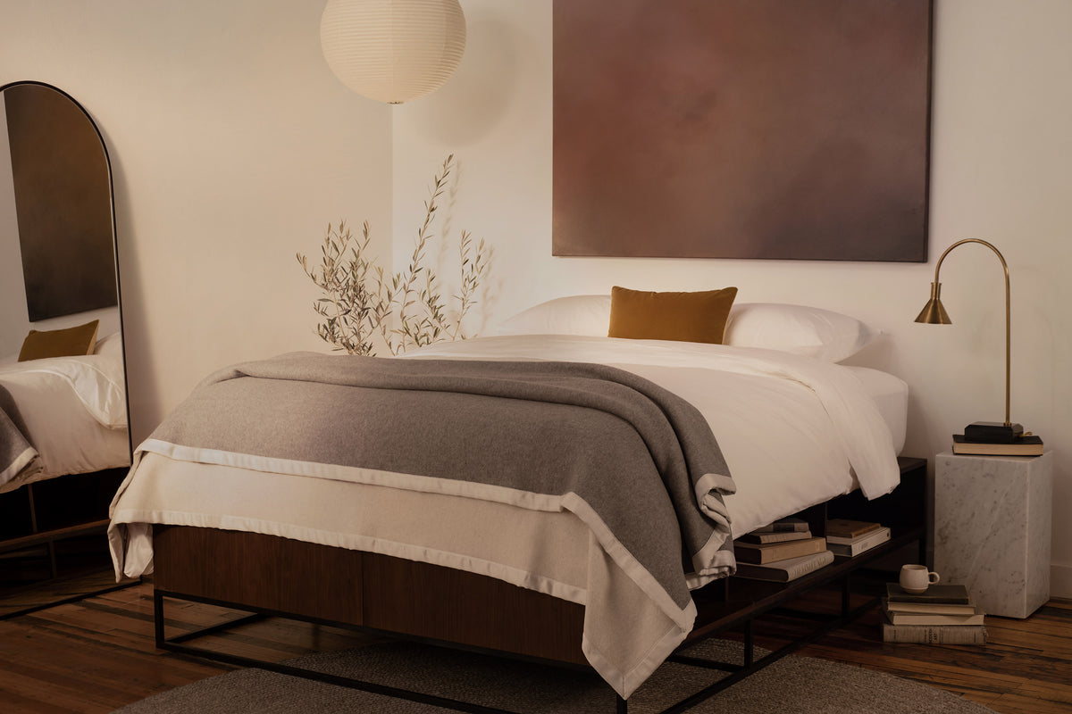 A bedroom with contemporary art and a bed made in LETTO 100% Organico Cotton Percale sheets, a gray Monte Bianco cashmere blanket, and orange velvet throw pillow. data-image-id=
