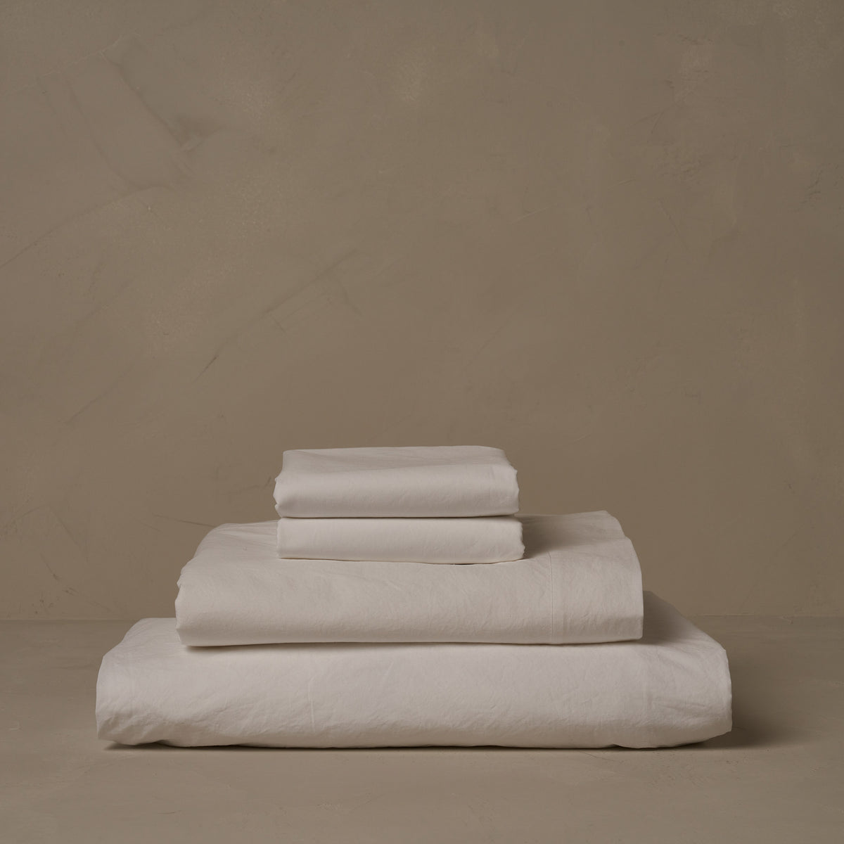 A stack of crisp and cool LETTO 100% Organic Cotton Percale sheets in white, made in Italy. The sheet set includes a fitted sheet, a flat sheet, and a pair of pillowcases. data-image-id=