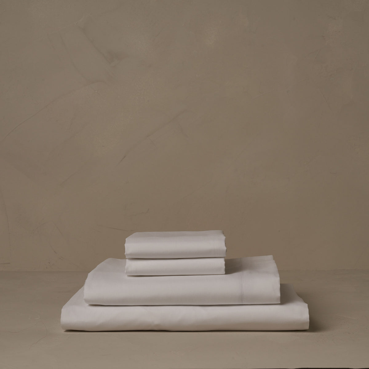 A stack of ultra soft and cool LETTO Sea Island Cotton Percale sheets in white, made in Italy. The sheet set includes a fitted sheet, a flat sheet, and a pair of pillowcases. data-image-id=